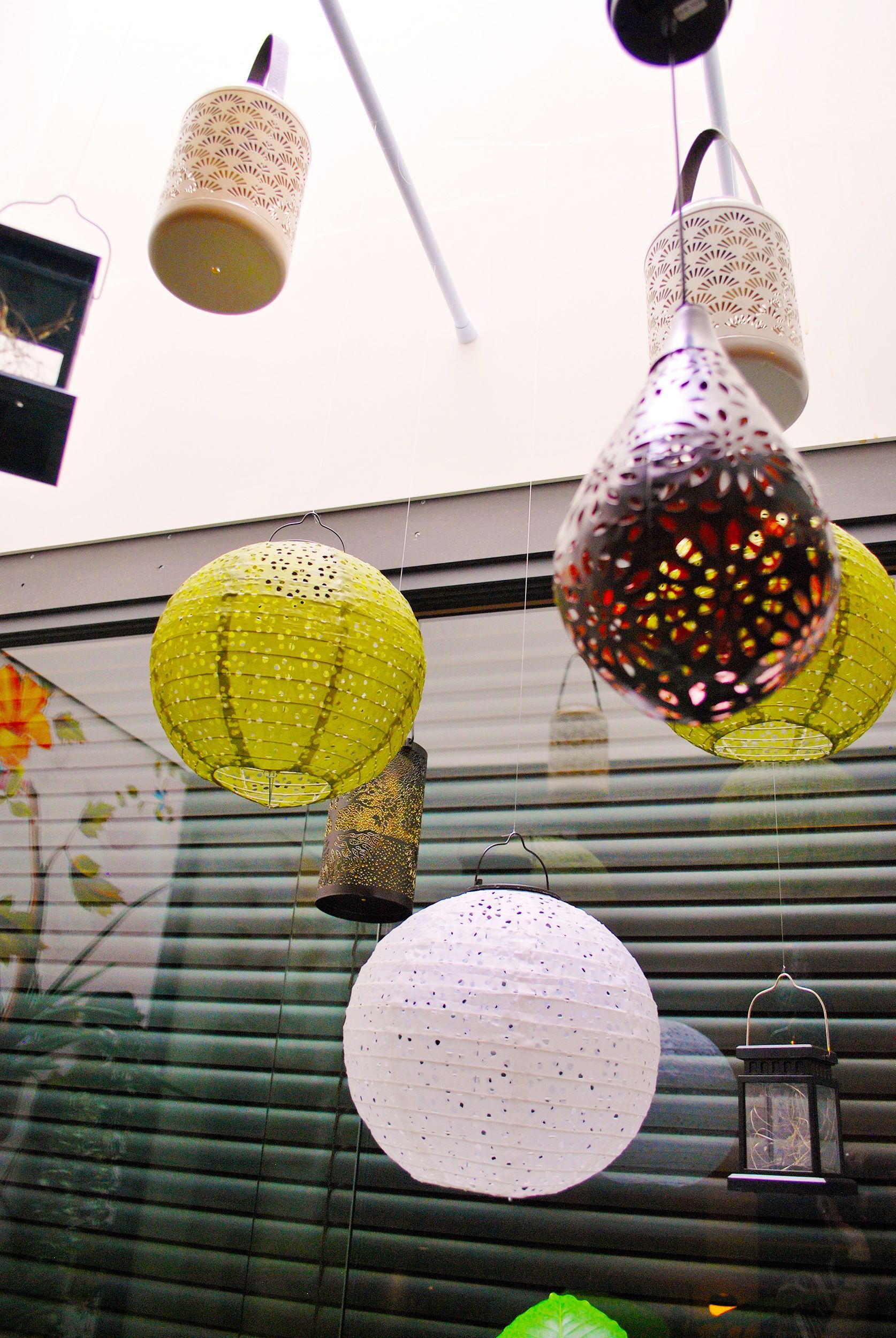 Een verzameling diverse decoratieve hanglantaarns, waaronder bolvormige papieren lantaarns en lantaarns met ingewikkelde metalen ontwerpen, in een kamer.