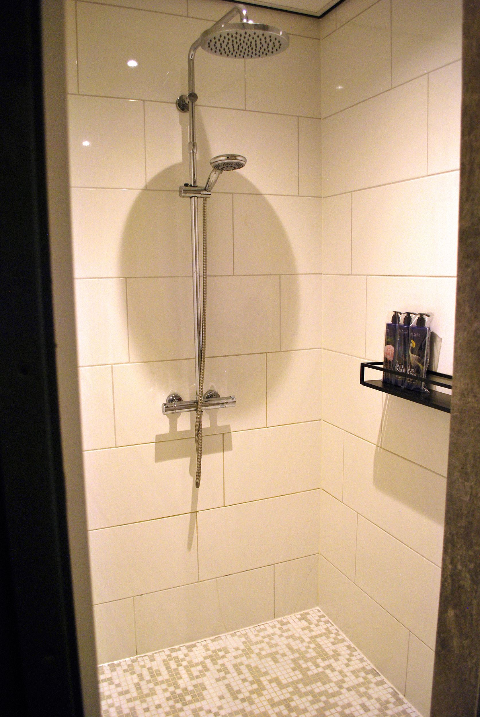 Een moderne douchecabine met witte metro-tegels op de wanden, een chromen regendouchekop en een plankje met toiletartikelen.