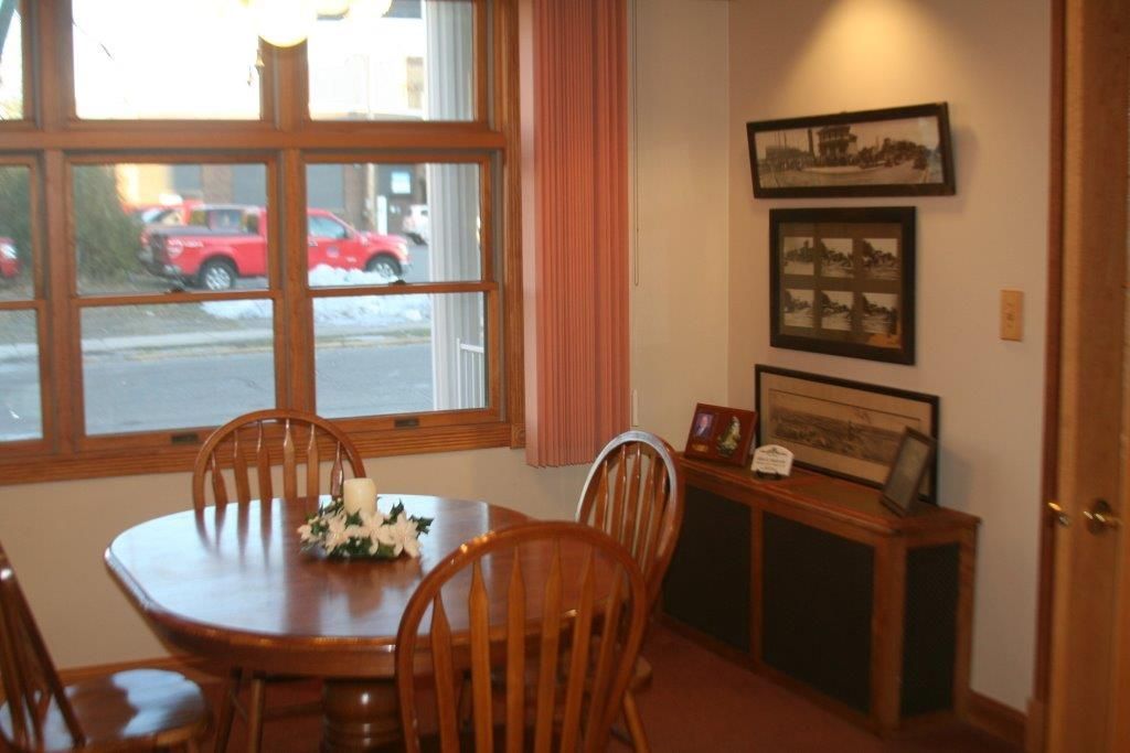 Dining room with wooden table and chairs by a window, pink curtain, artwork on the wall, and a red truck visible outside.