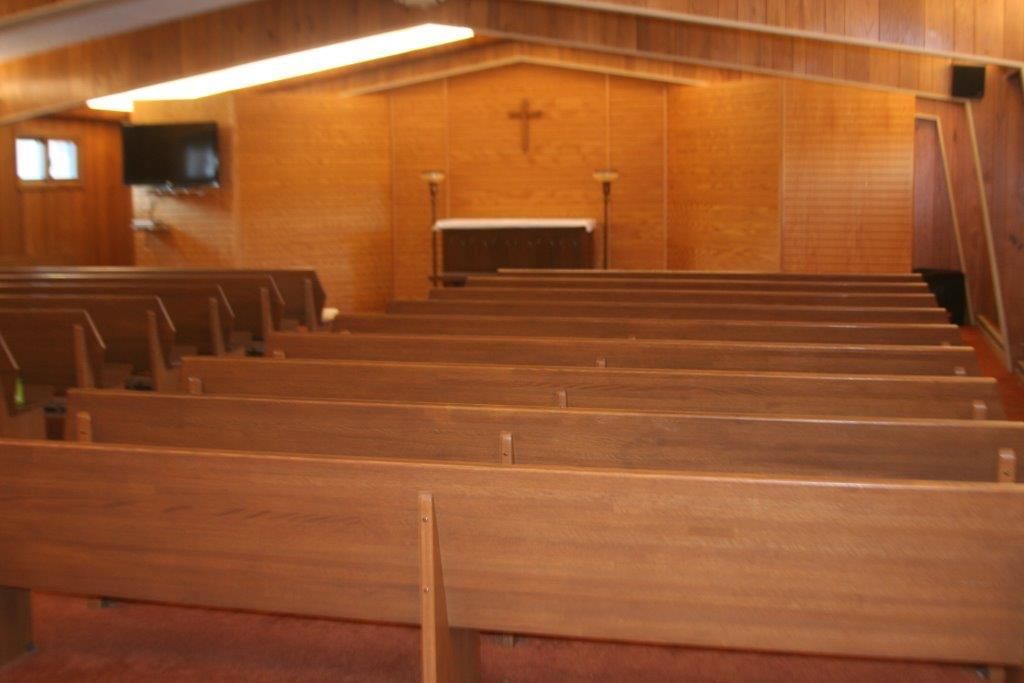 Interior view of a chapel with wooden pews facing an altar with a cross.