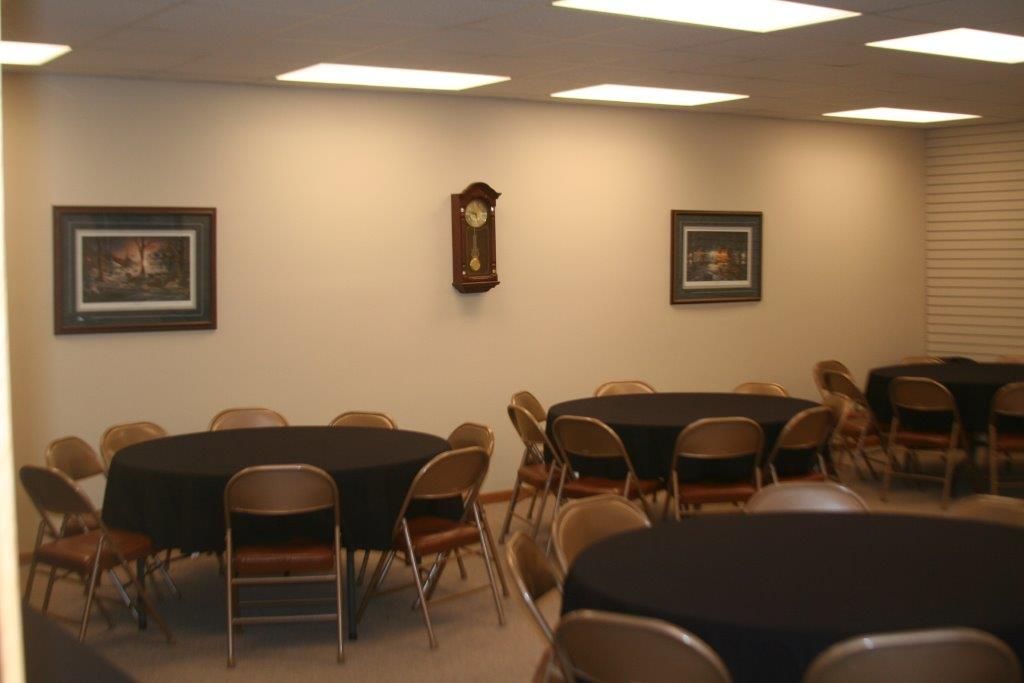 A room with round tables covered in black cloth, surrounded by chairs. Artwork and a clock hang on the wall.