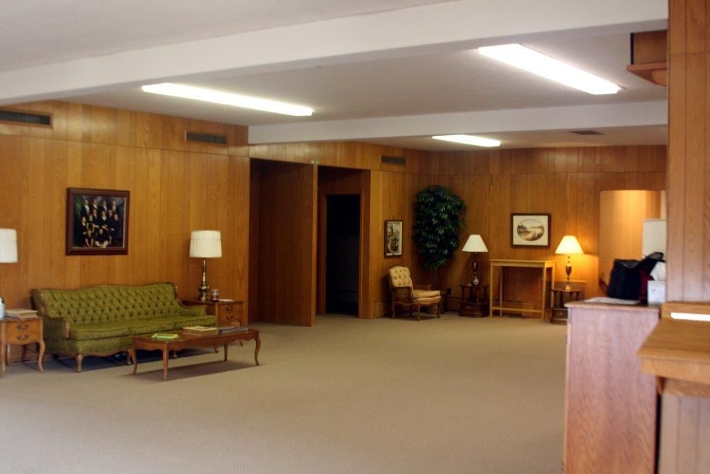 Reception area with wood paneling, green sofa, and a large plant.
