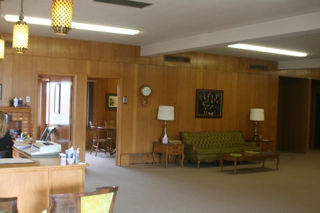 Reception area with wood paneling, green sofa, and two lamps. Desk visible at left.