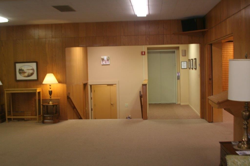 Hallway with beige carpet, wooden paneling, stairs, and an elevator.