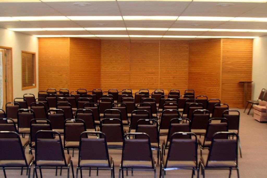 Empty auditorium with rows of chairs facing a wooden wall.