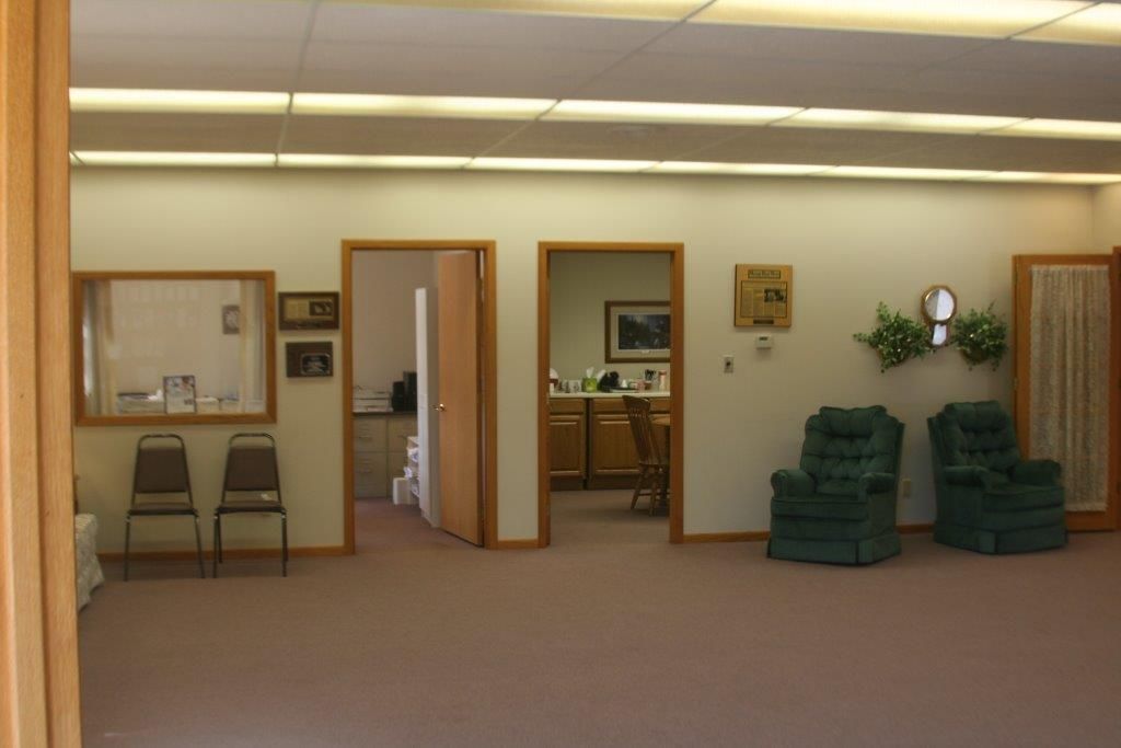 Interior of a waiting room with two green armchairs, three doorways, and two chairs.