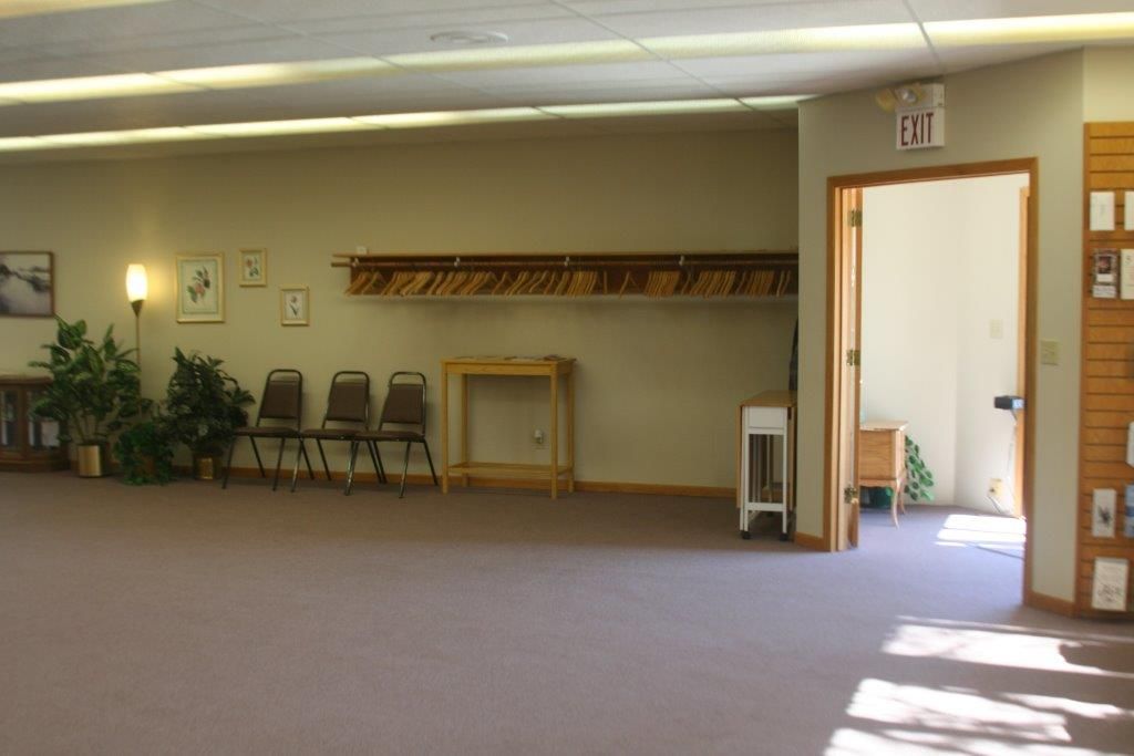 Empty room with chairs, coat rack, and open doorway; light brown walls, beige carpet.