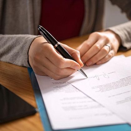 Hand signing a document with a black pen on a wooden table
