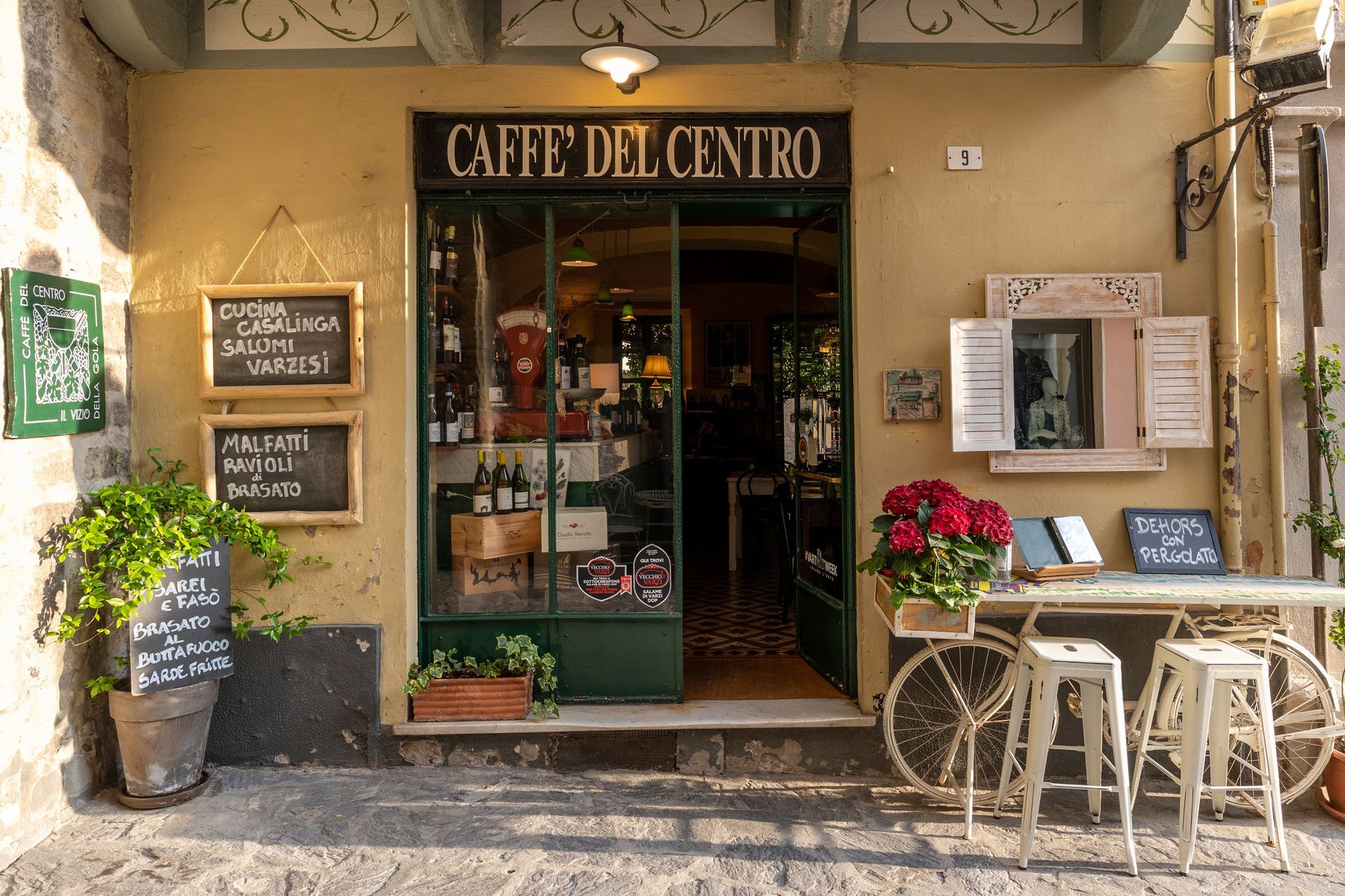Cafe entrance with open door, blackboards, flowers, and bicycle-themed decor.