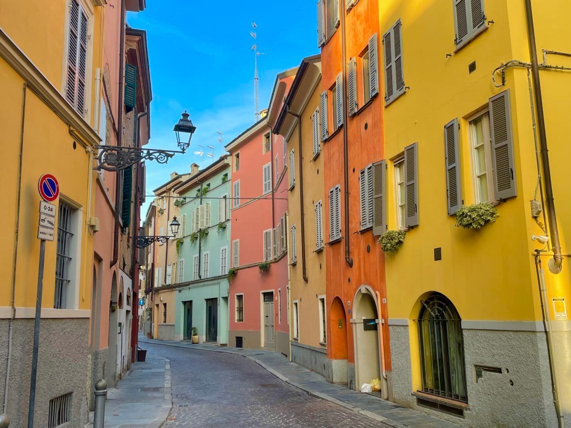 Colorful buildings line a cobblestone street in Italy, under a bright blue sky.