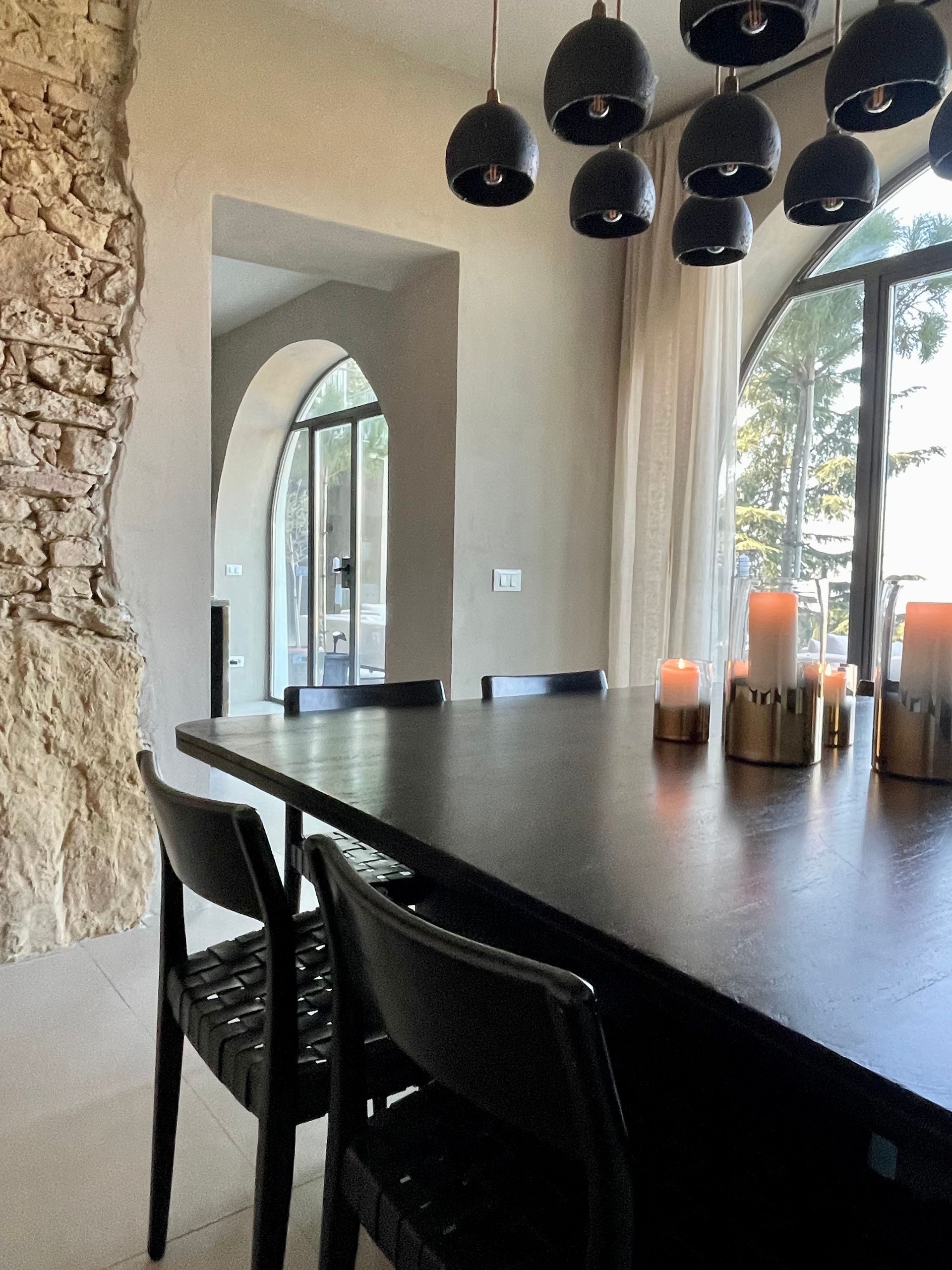 Dining room with black table, chairs, and hanging lights, arched doorways, and stone wall.
