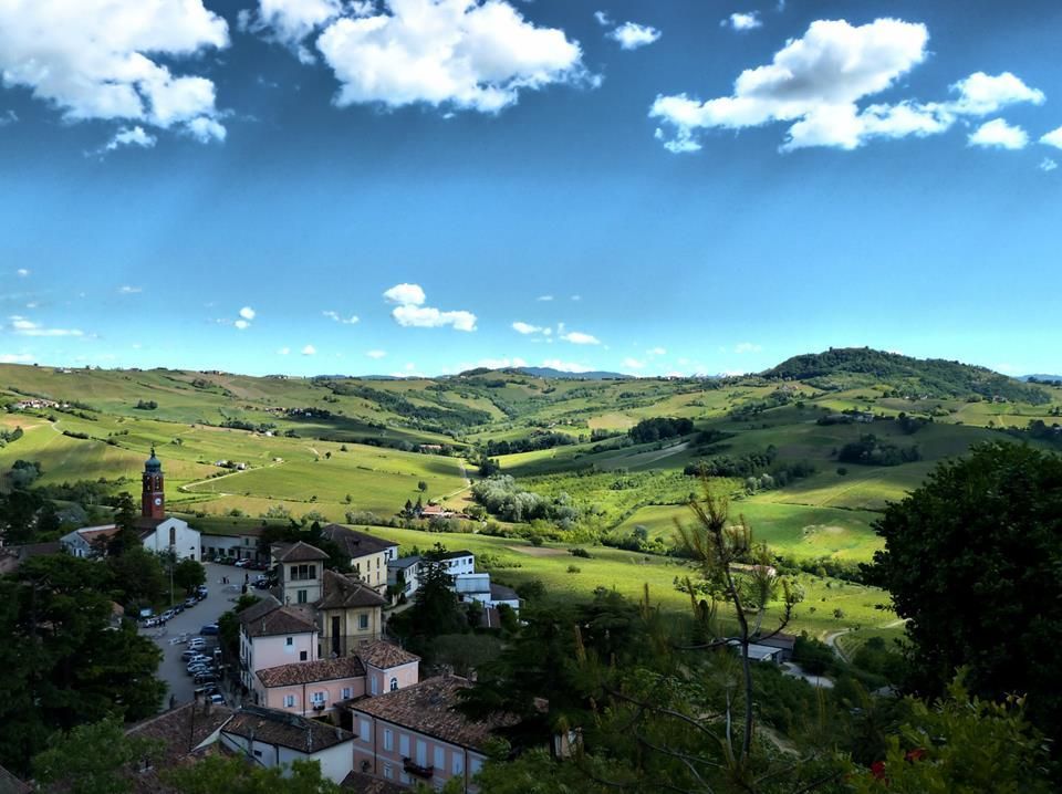 Rolling green hills with a village and church under a bright blue sky with fluffy clouds.