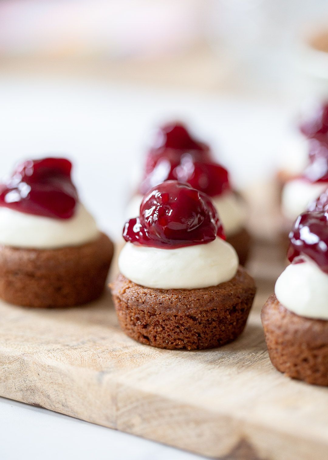 Mini chocolate cupcakes topped with white cream and cherry compote on a wooden board.