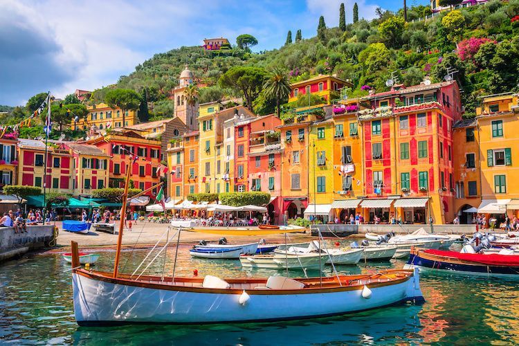 Colorful buildings line a harbor in Portofino, Italy, with boats floating and a lush hillside in the background.