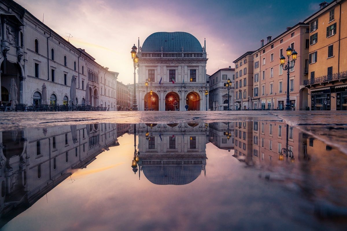 Reflection of an ornate building in a puddle on a city square at dawn.