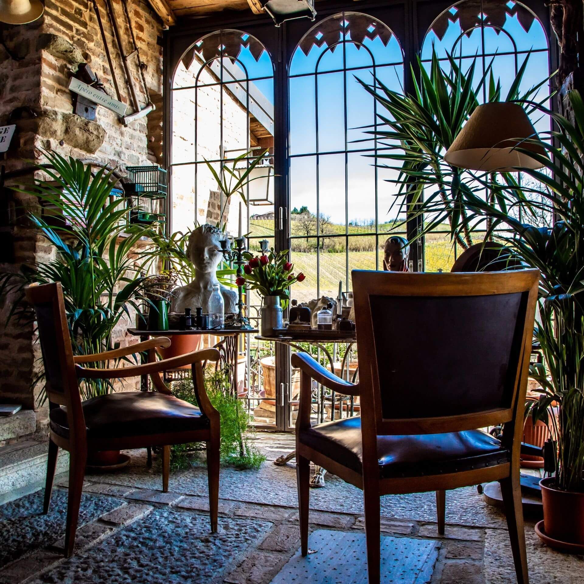 Two chairs face a table in a sunroom. Large arched windows look out at a hillside.
