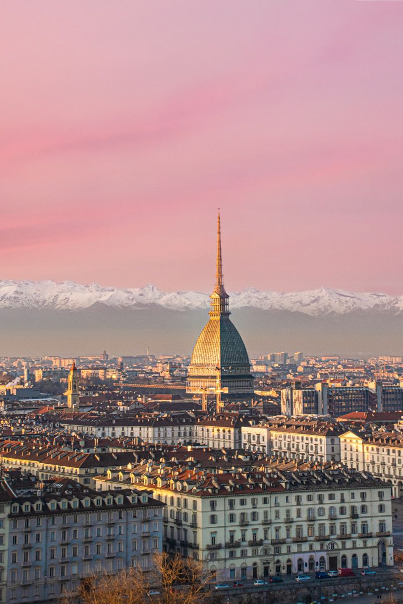 City skyline with Mole Antonelliana, under a pink sky, mountains in the background.