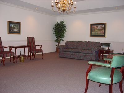 A waiting room with brown carpet, two chairs, a small table, a sofa, and artwork on the walls.