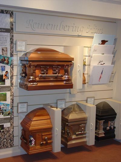 Wall display of polished wooden coffins in a funeral home showroom, with brochures on the side.