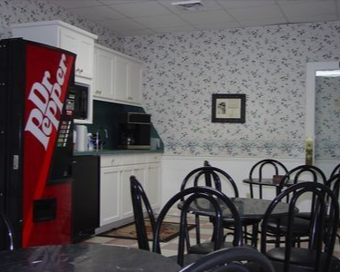Break room with Dr. Pepper vending machine, cabinets, table, and chairs. Floral wallpaper.