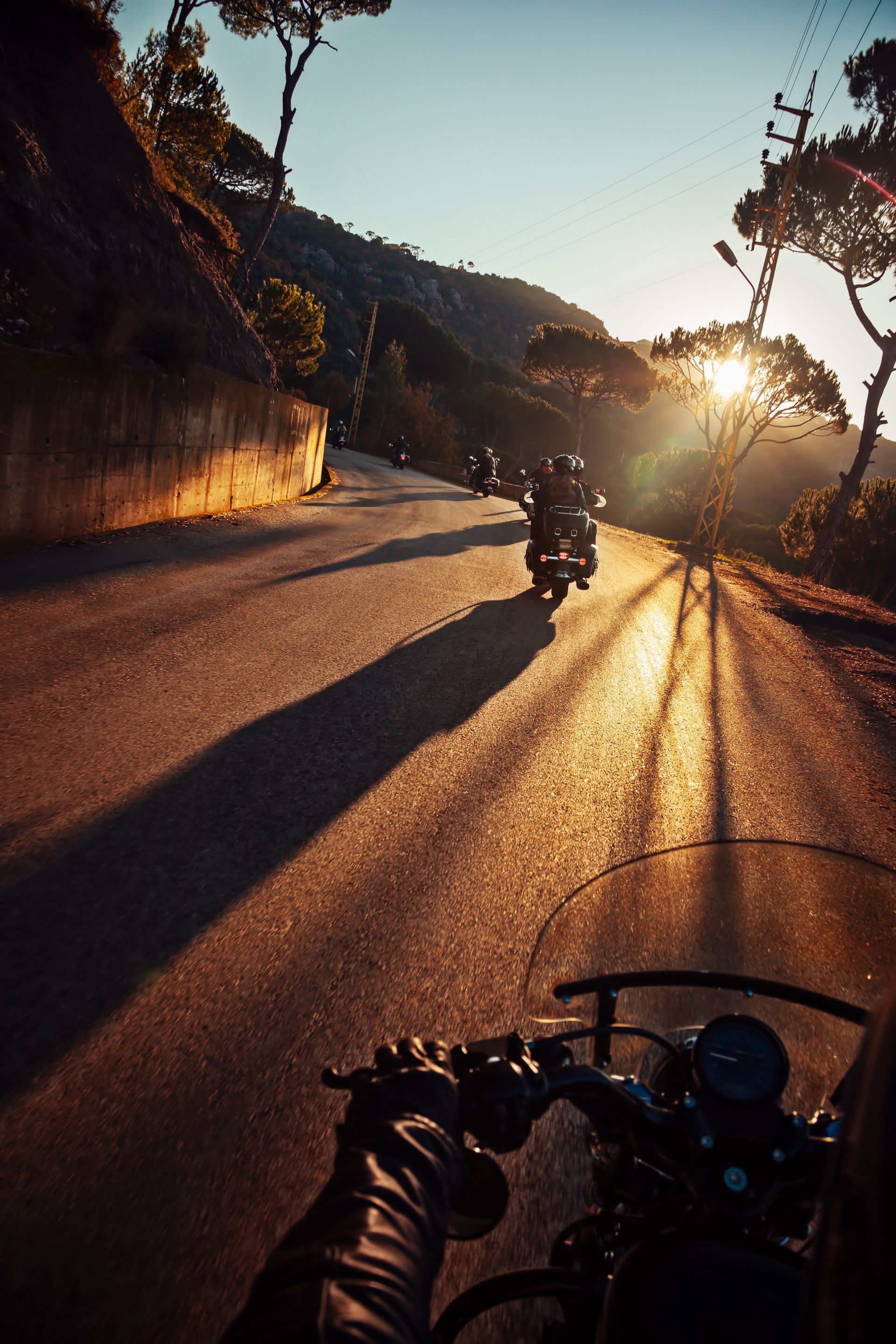 Motorcyclist's view on a road with several motorcycles ahead, bathed in golden sunlight from the setting sun.