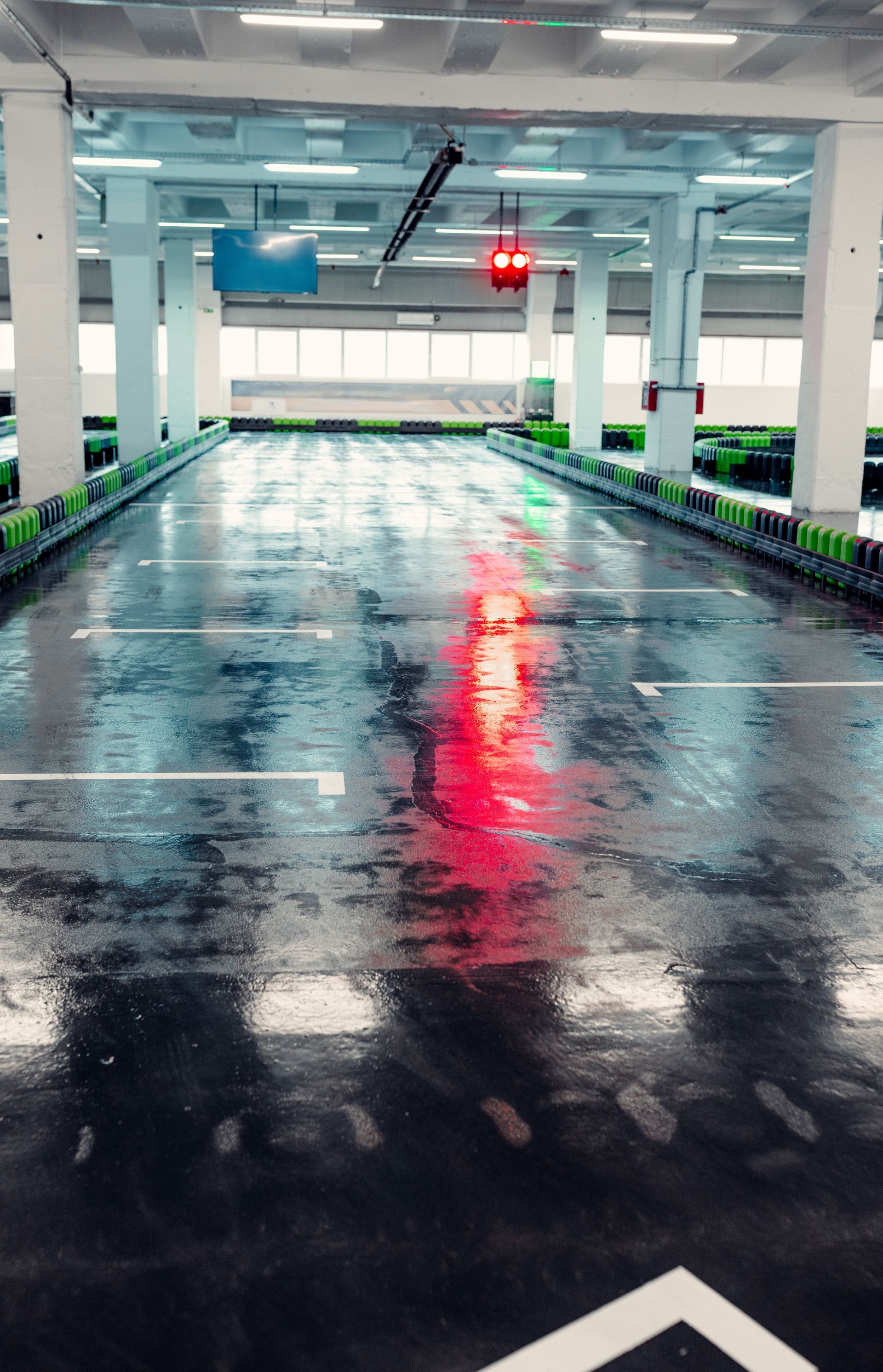 Empty indoor parking garage with wet, reflective floor, red light at end.