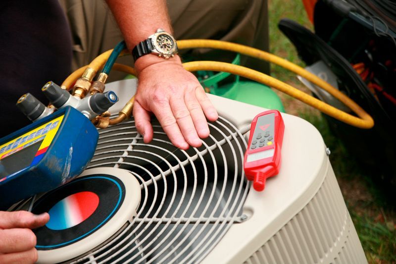 Person working on an air conditioner unit. They are using gauges, a hose, and a red thermometer.