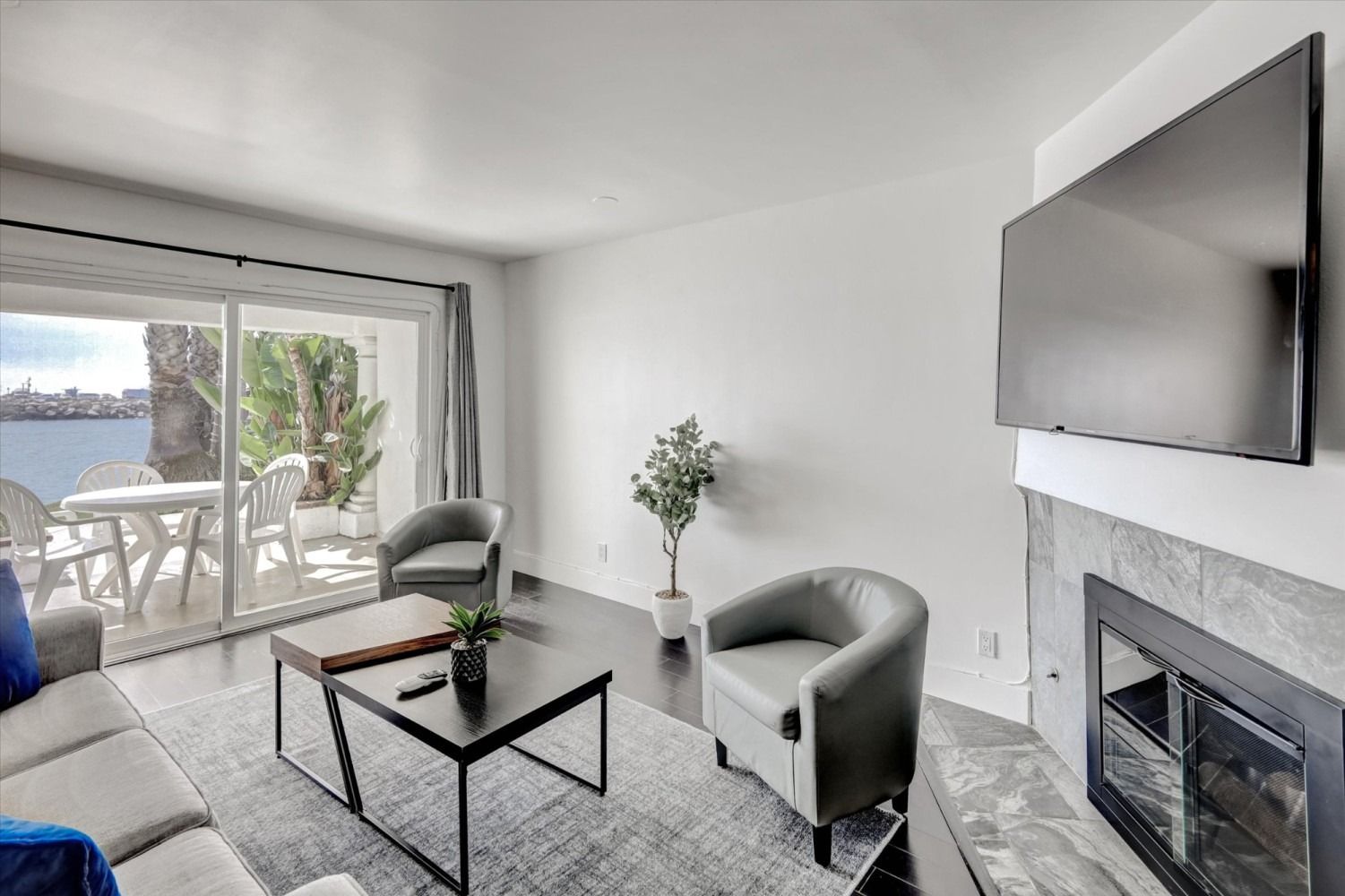 A living room with a gray sofa, two gray chairs, a coffee table, a fireplace with a mounted TV, and a sliding glass door.