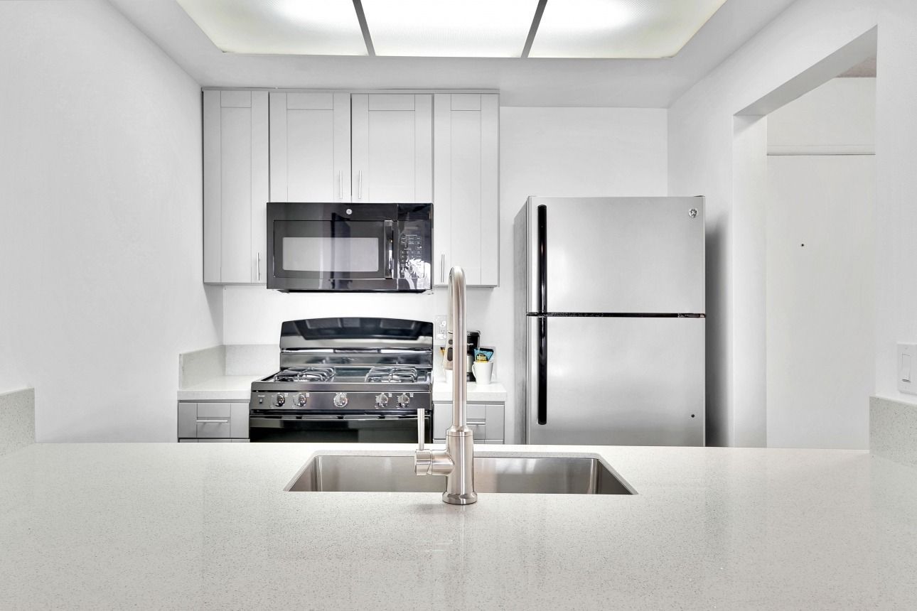 A bright, modern kitchen featuring a white quartz countertop, stainless steel appliances, and minimalist white cabinets.