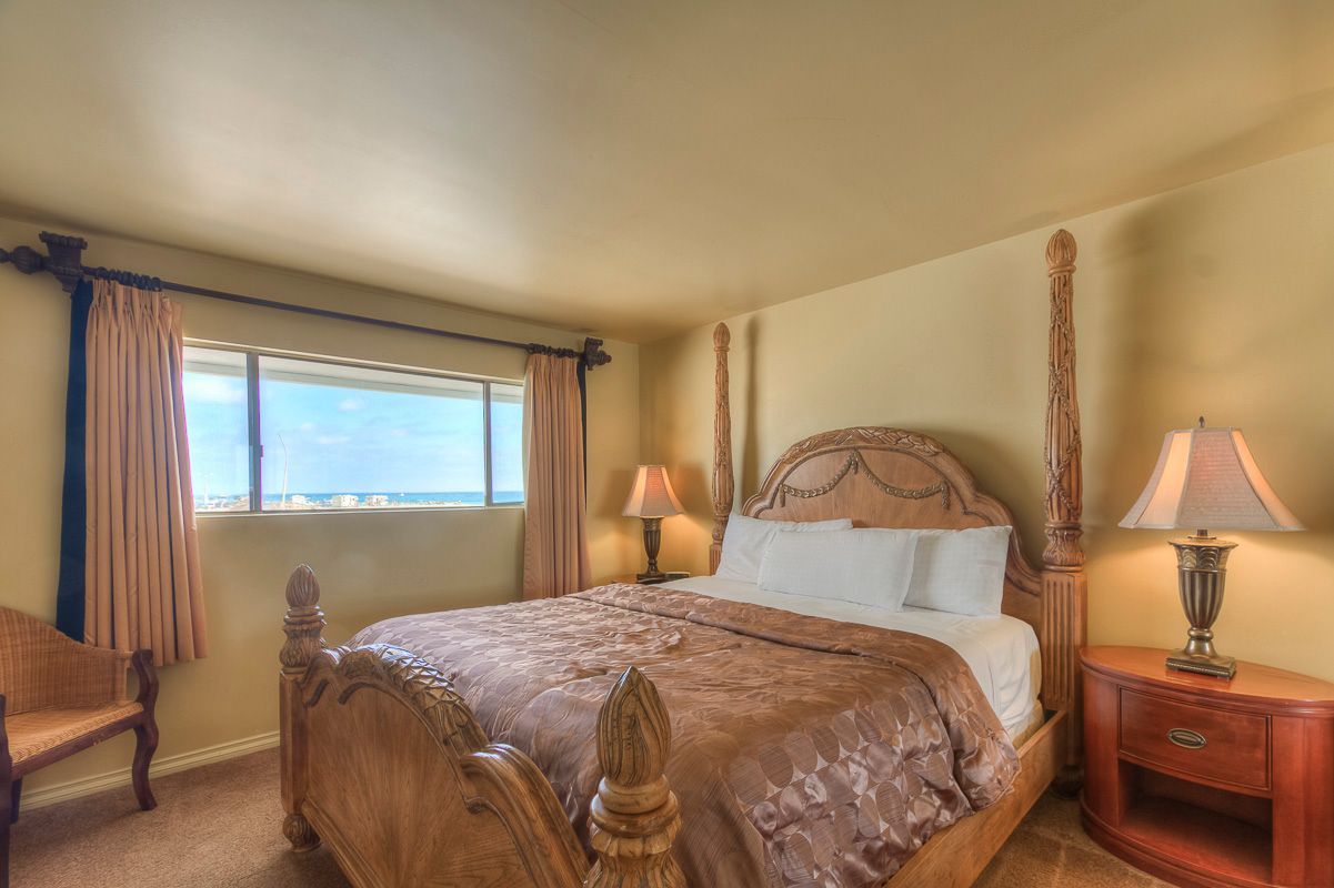 Bedroom with a large bed, nightstand, small window, and tan walls.