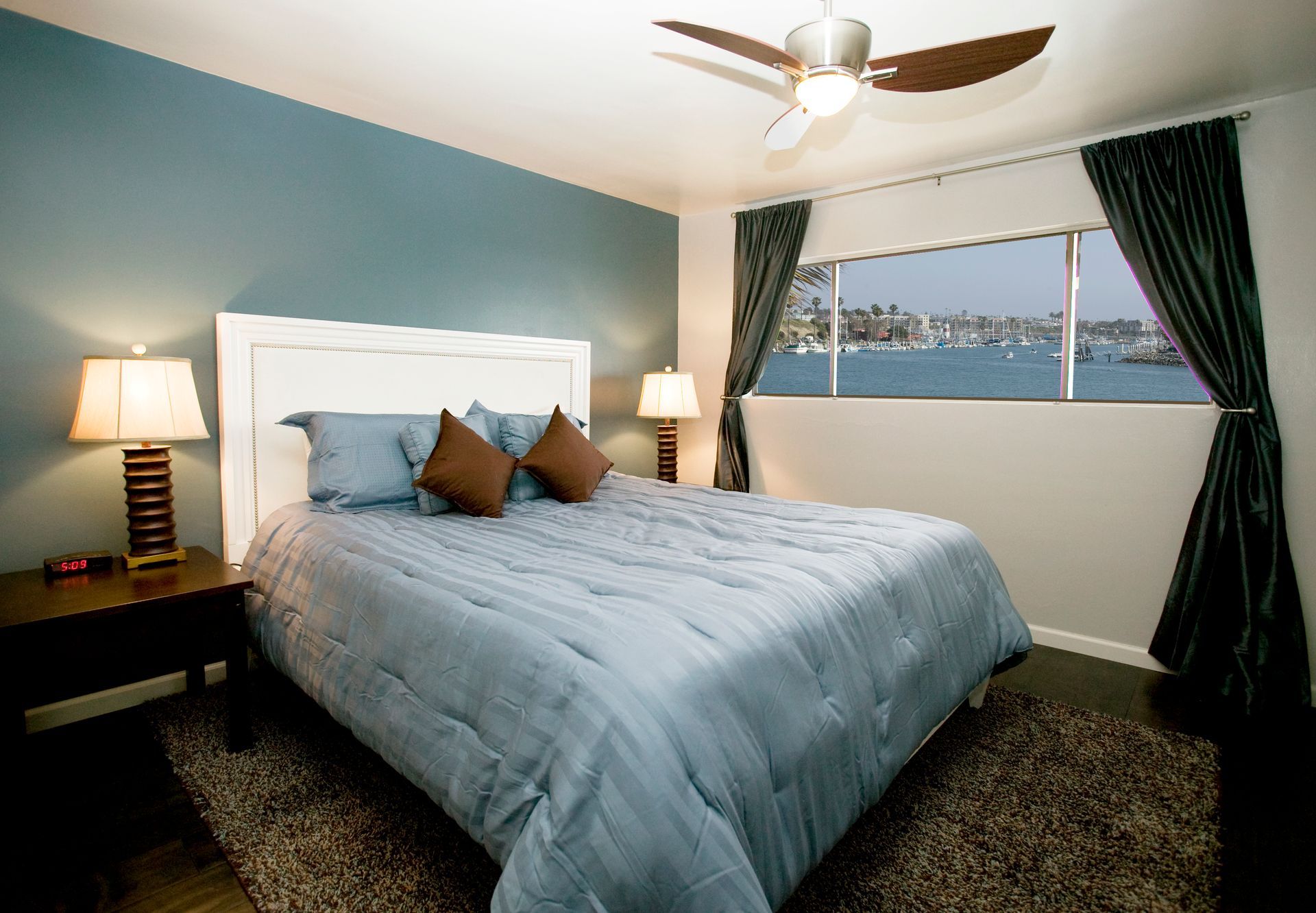Bedroom with blue wall, bed, nightstands, window with a view, and dark curtains.