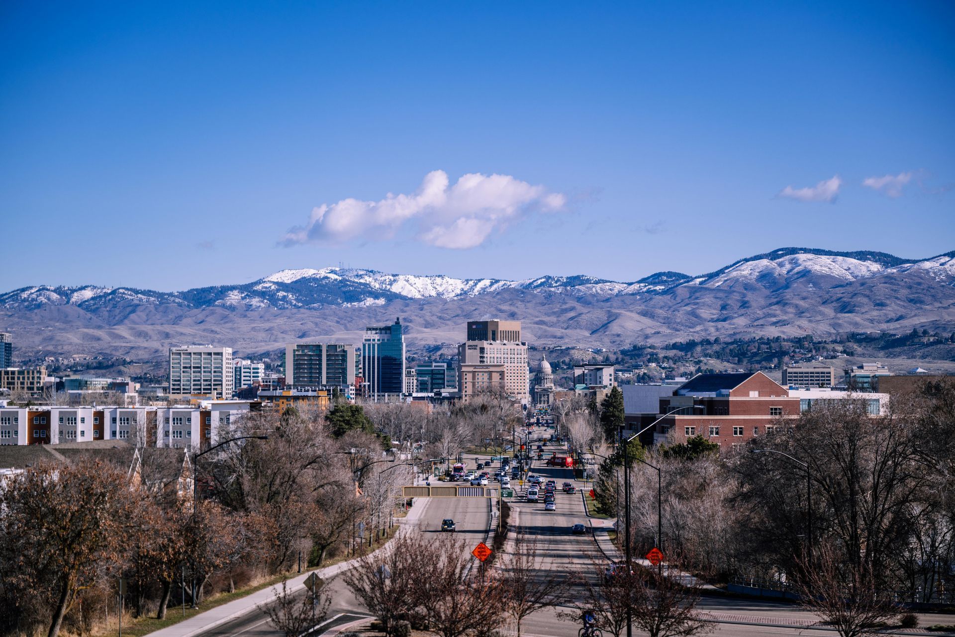 A scenic view of the Boise, Idaho skyline featuring modern buildings against a backdrop of snow-capped mountains.