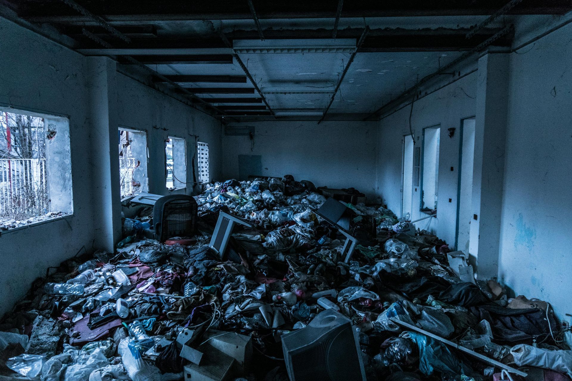 A dimly lit, dilapidated room filled with a massive pile of scattered trash, debris, and discarded items.
