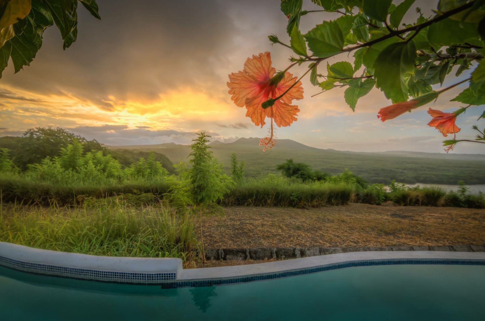 Sunset over a pool and green valley, with orange leaves framing the view