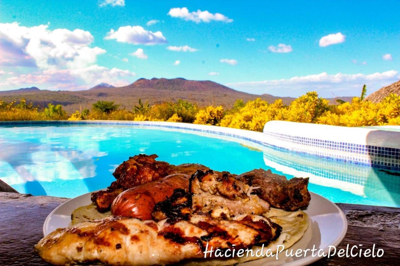 Plate of grilled meat by a turquoise pool with mountains and blue sky in the background