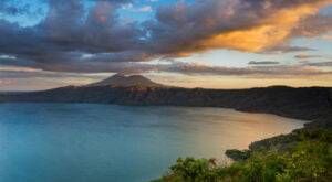 Sunset over a calm blue bay with a mountain silhouette and glowing clouds