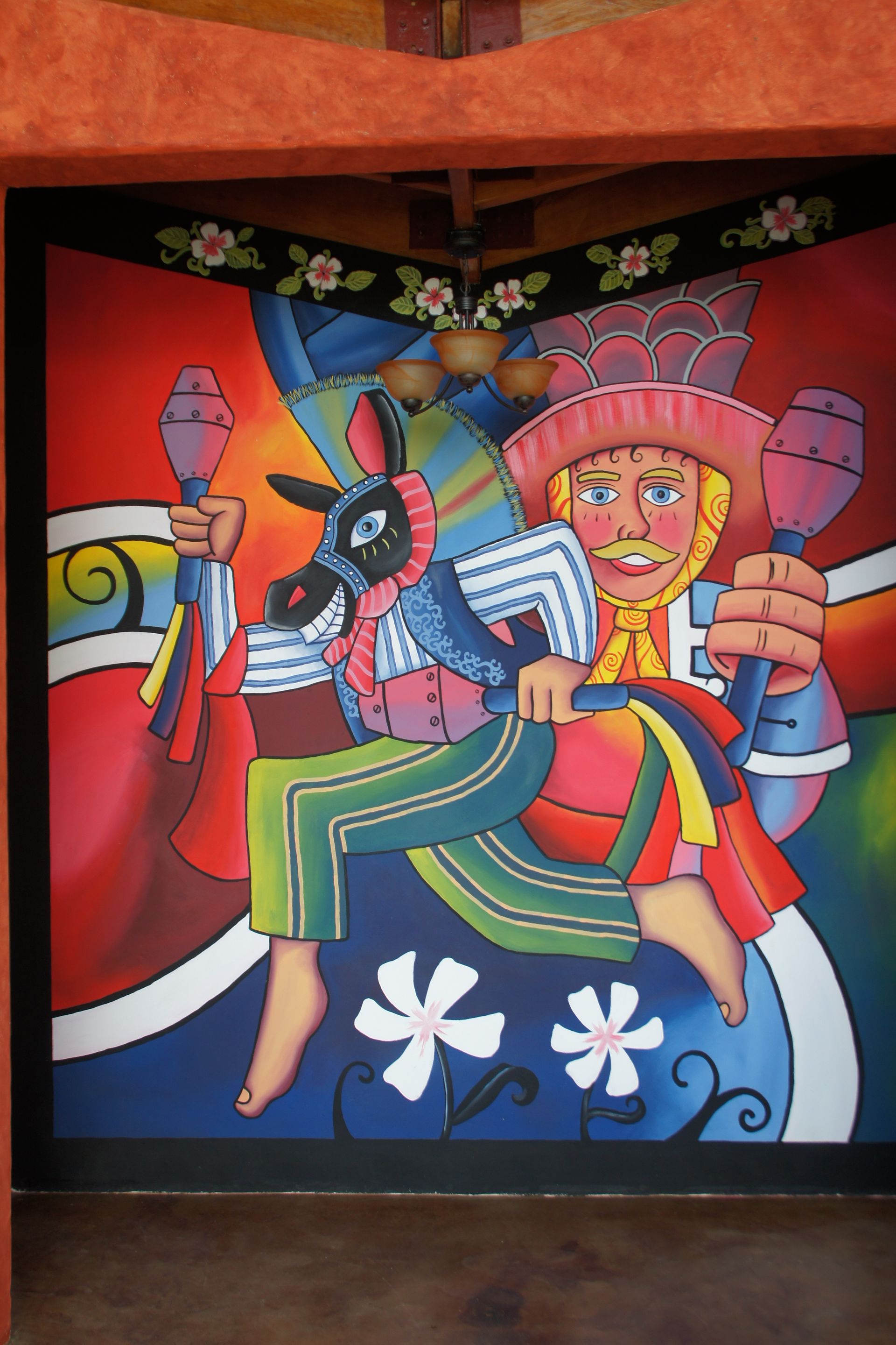 Colorful mural of a smiling figure in traditional clothing riding a horse with flowers and birds on a dark wall
