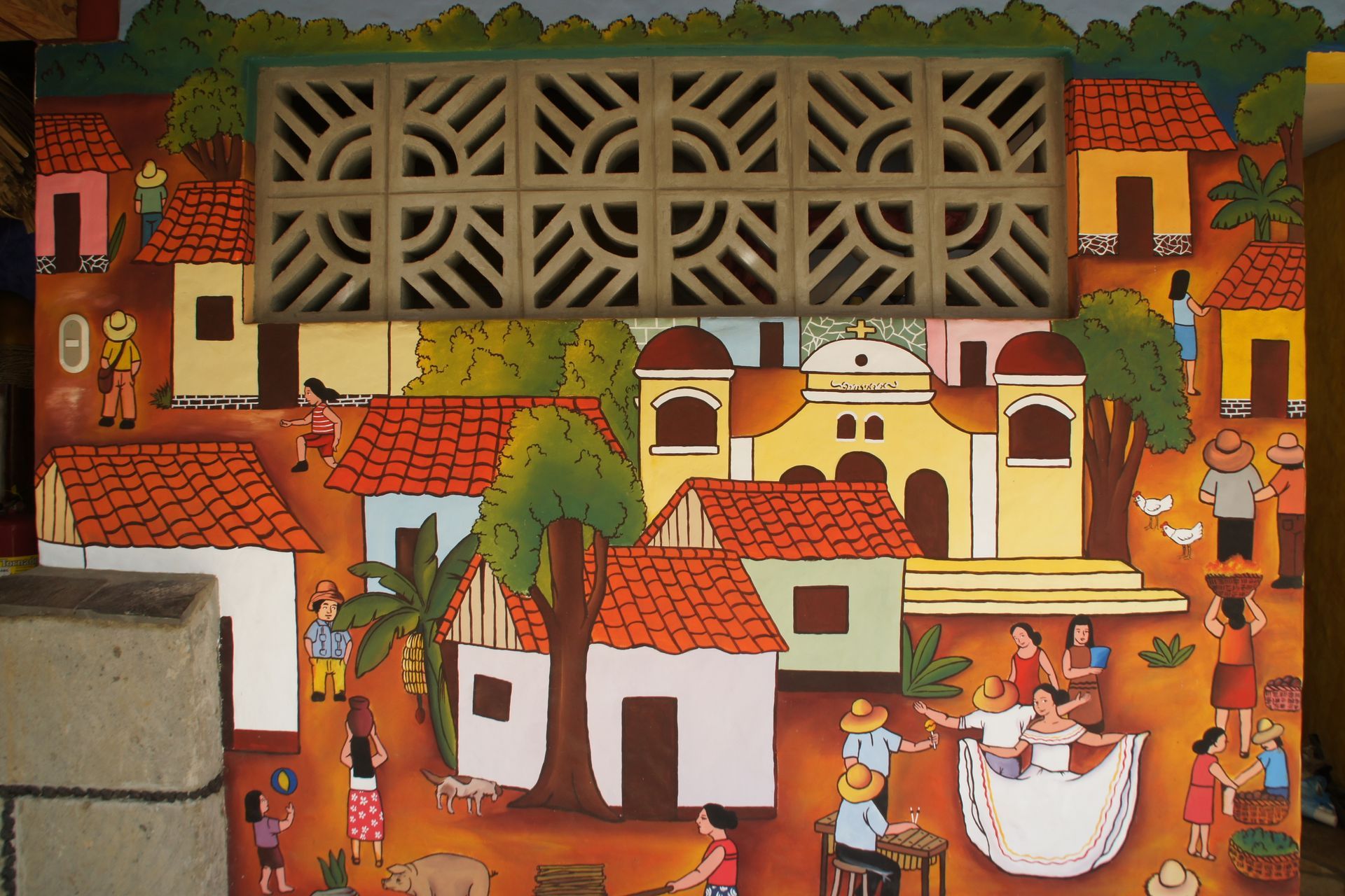 Colorful mural of a village with red roofs, trees, and people gathered in a courtyard around a table