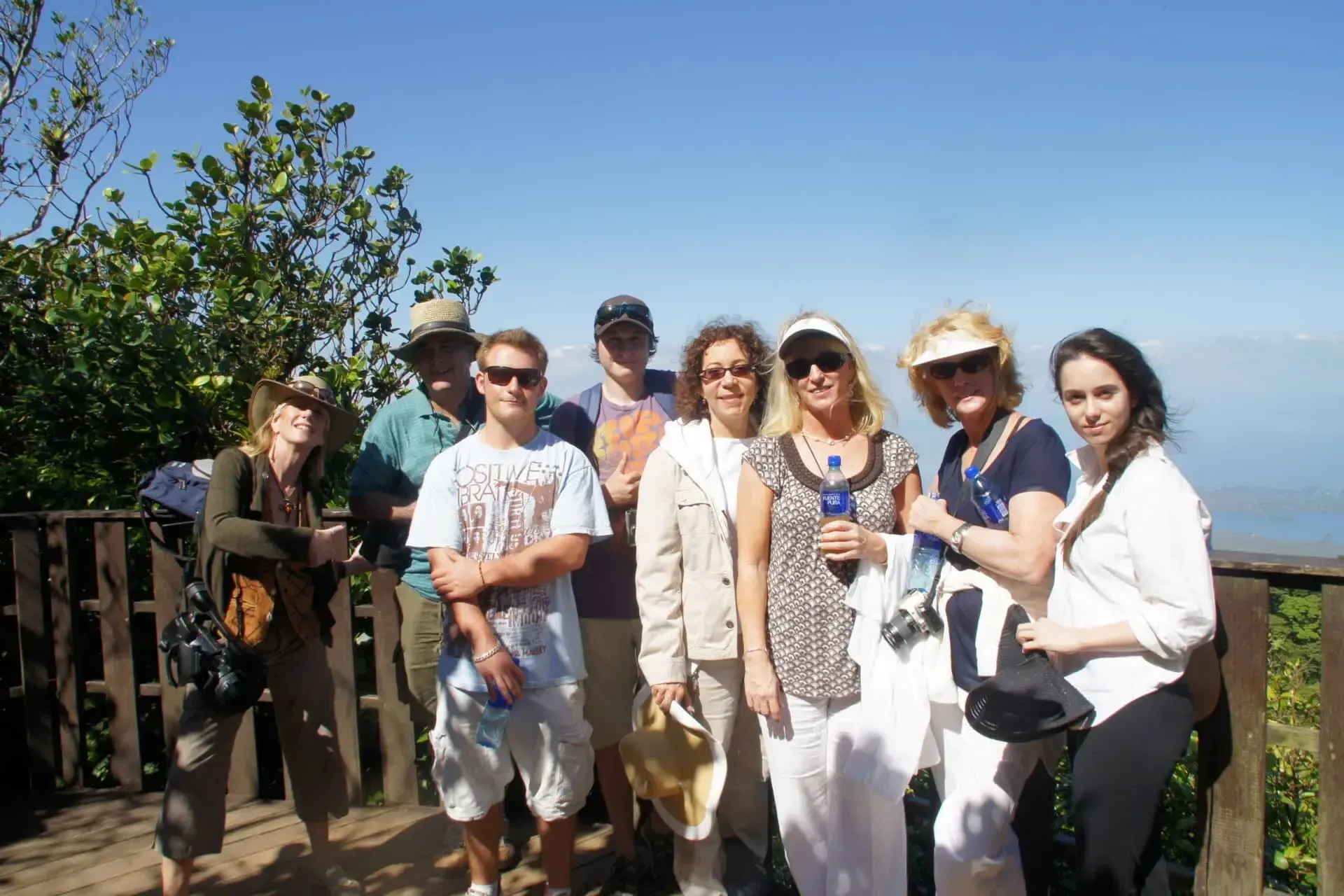 Group of friends posing outdoors on a sunny lookout, with blue sky and ocean in the background.