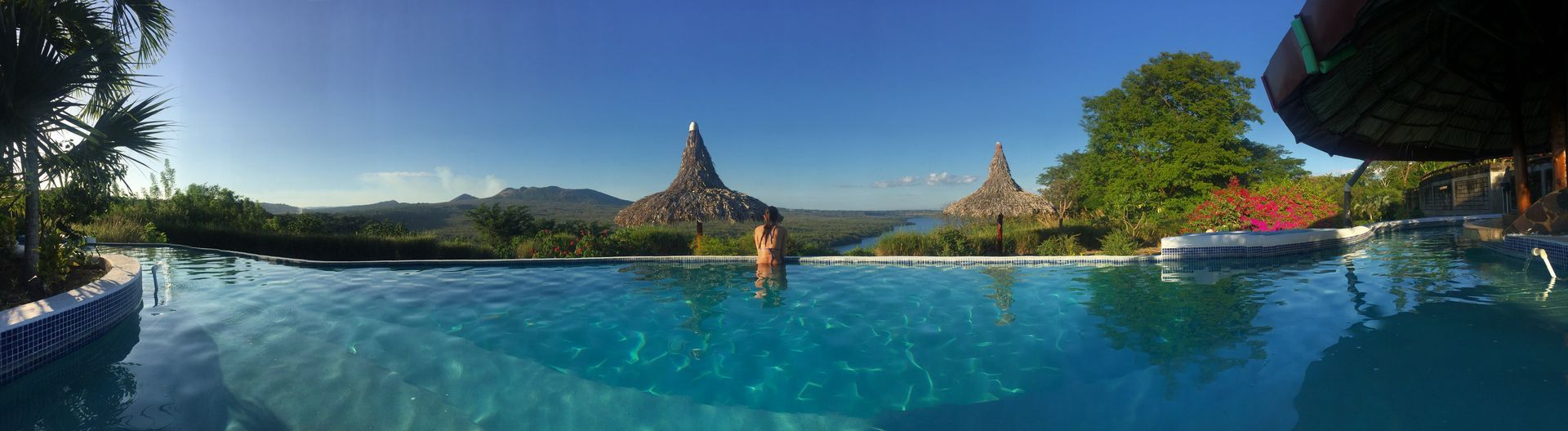 Panoramic resort pool with turquoise water, palm trees, and a temple-like pagoda under a clear blue sky