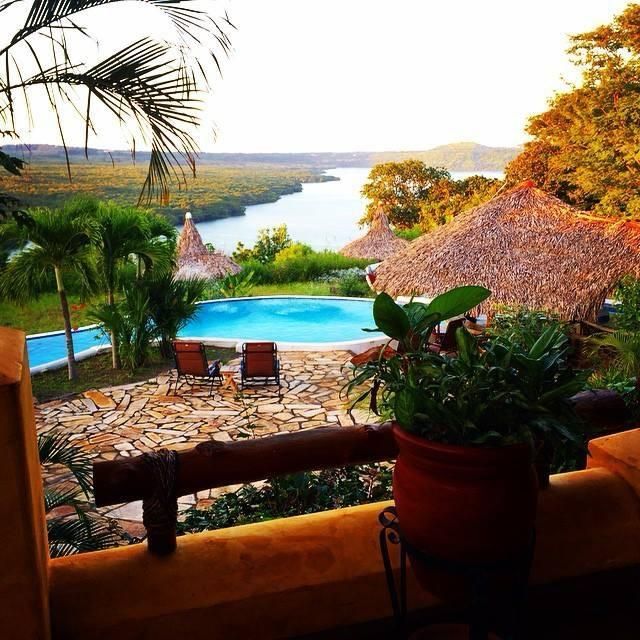 Tropical resort terrace with pool, palms, thatched roofs, and a river view at sunset