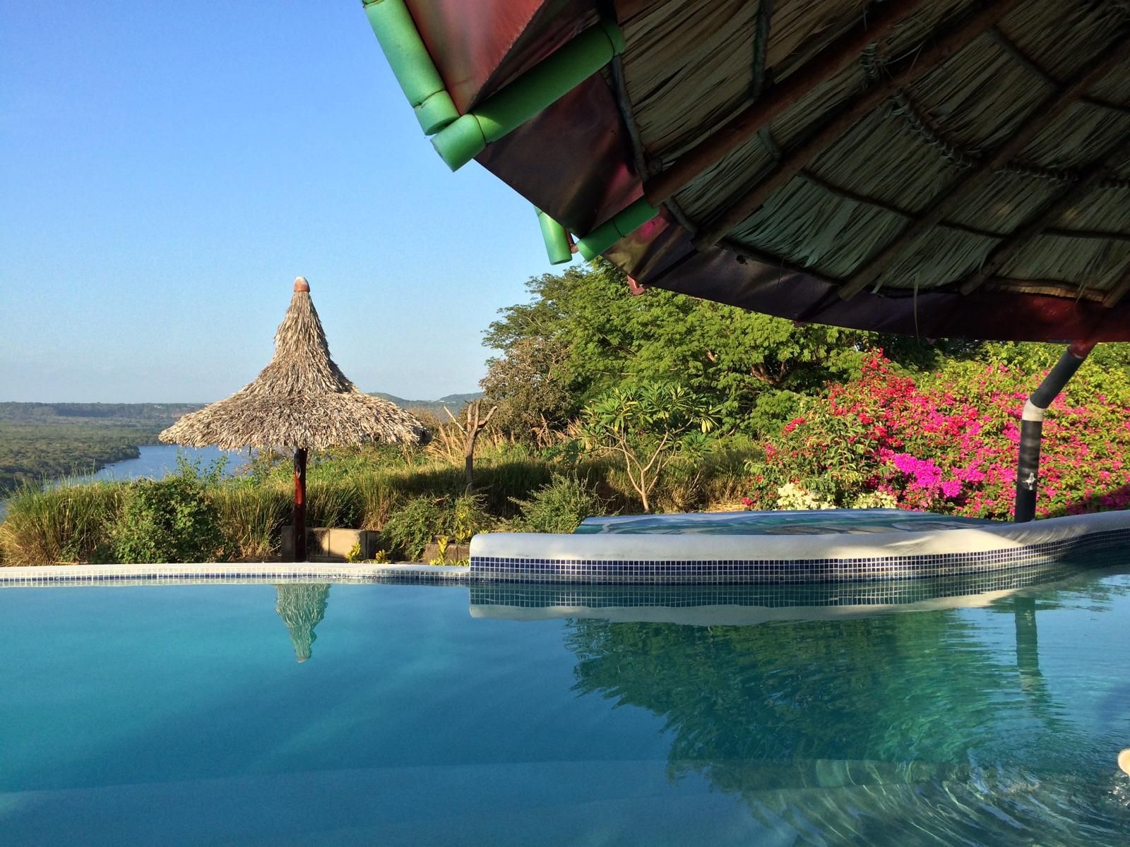 Infinity pool overlooking a tropical bay with a thatched hut and lush greenery at sunset
