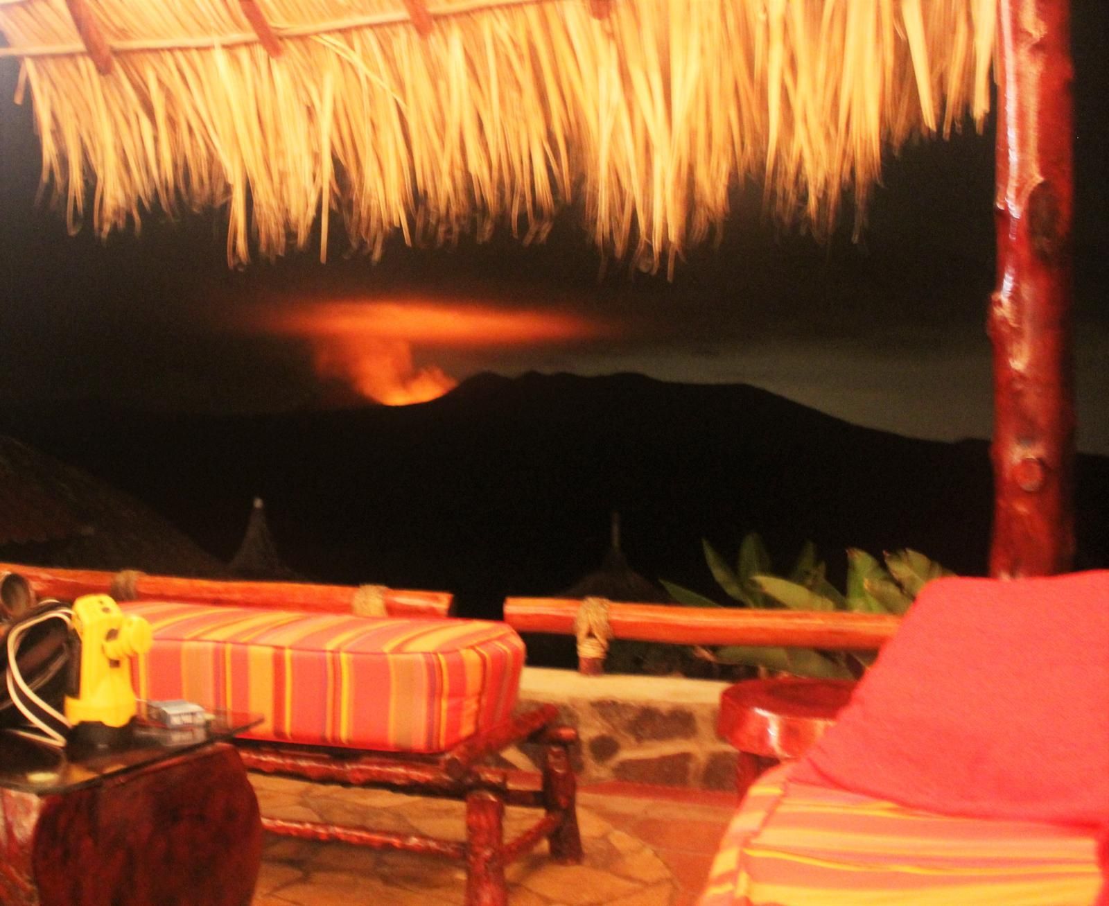 Thatched hut lounge at sunset with striped cushions and a dark mountain silhouette in the background