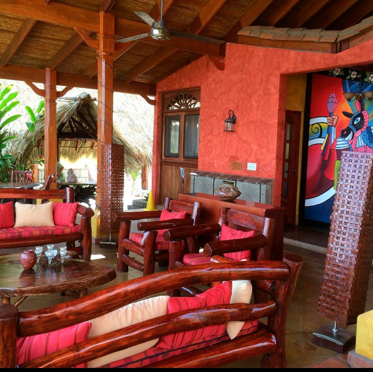 Open-air porch with red brick walls, wooden furniture, and colorful artwork under a wood ceiling