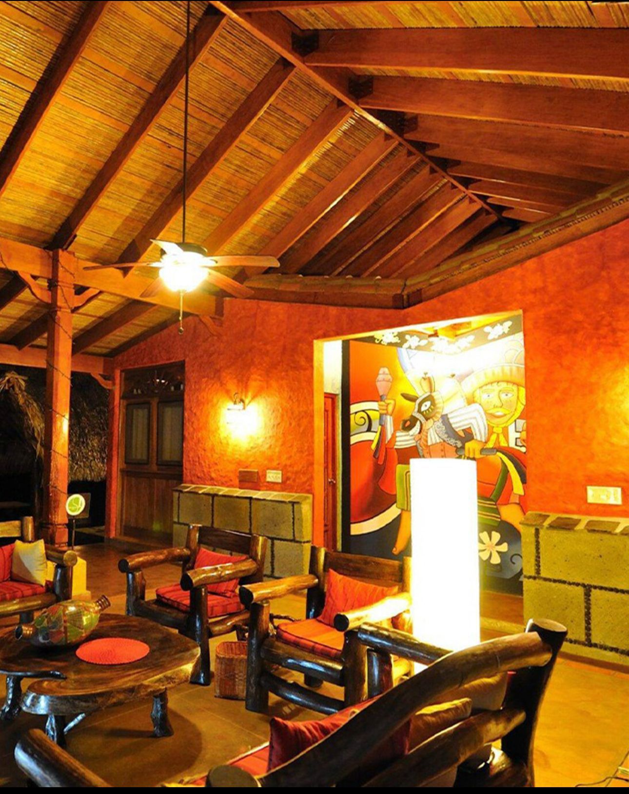 Warm, rustic lounge with wooden beams, orange walls, leather chairs, and ambient lighting.