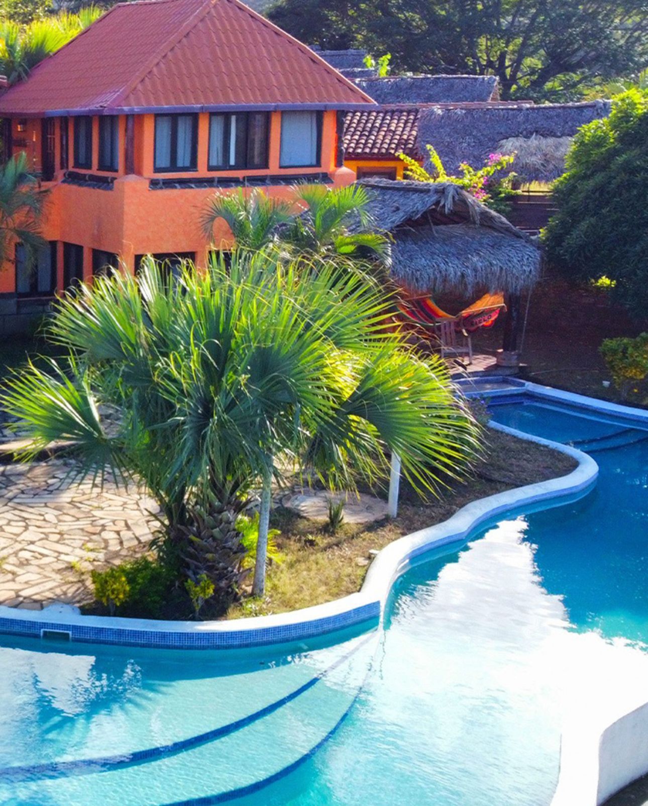 Orange villa with tiled roof beside a blue swimming pool and tropical palm trees