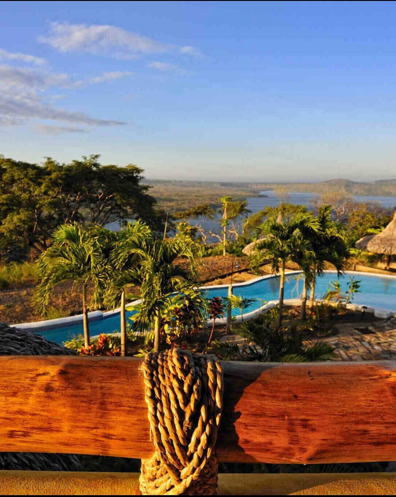 Poolside view from a wooden deck overlooking palm trees, mountains, and a wide valley under a blue sky.