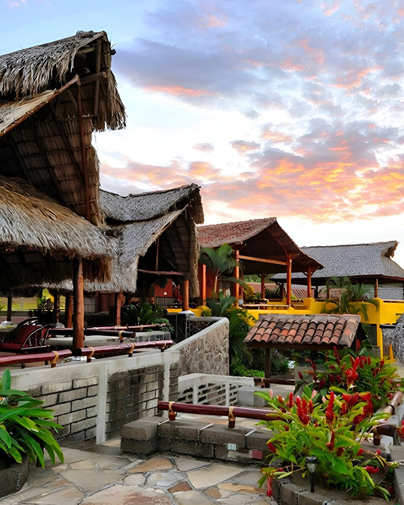 Thatched-roof tropical resort villas at sunset with stone paths and lush greenery