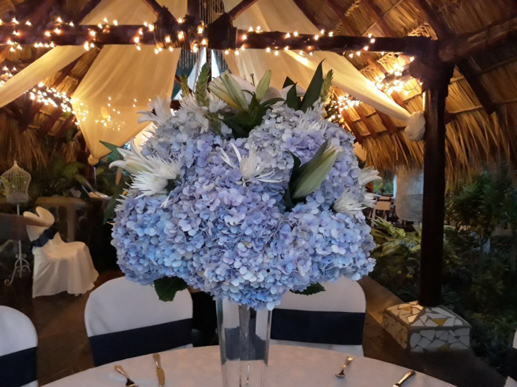 Blue hydrangea bouquet in a vase on a table under warm string lights in a rustic venue