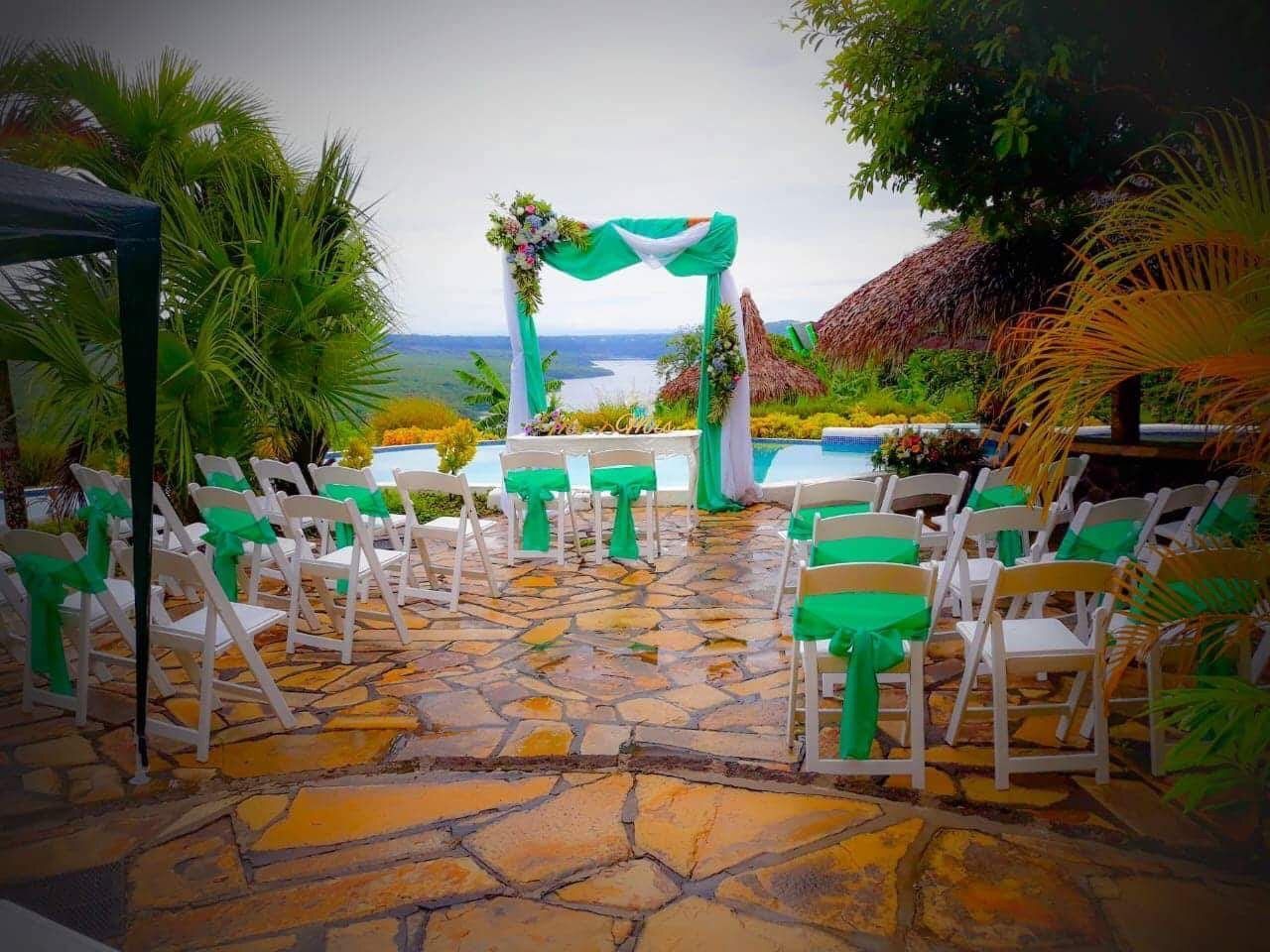 Outdoor wedding aisle with white chairs, green drapes, and ocean view
